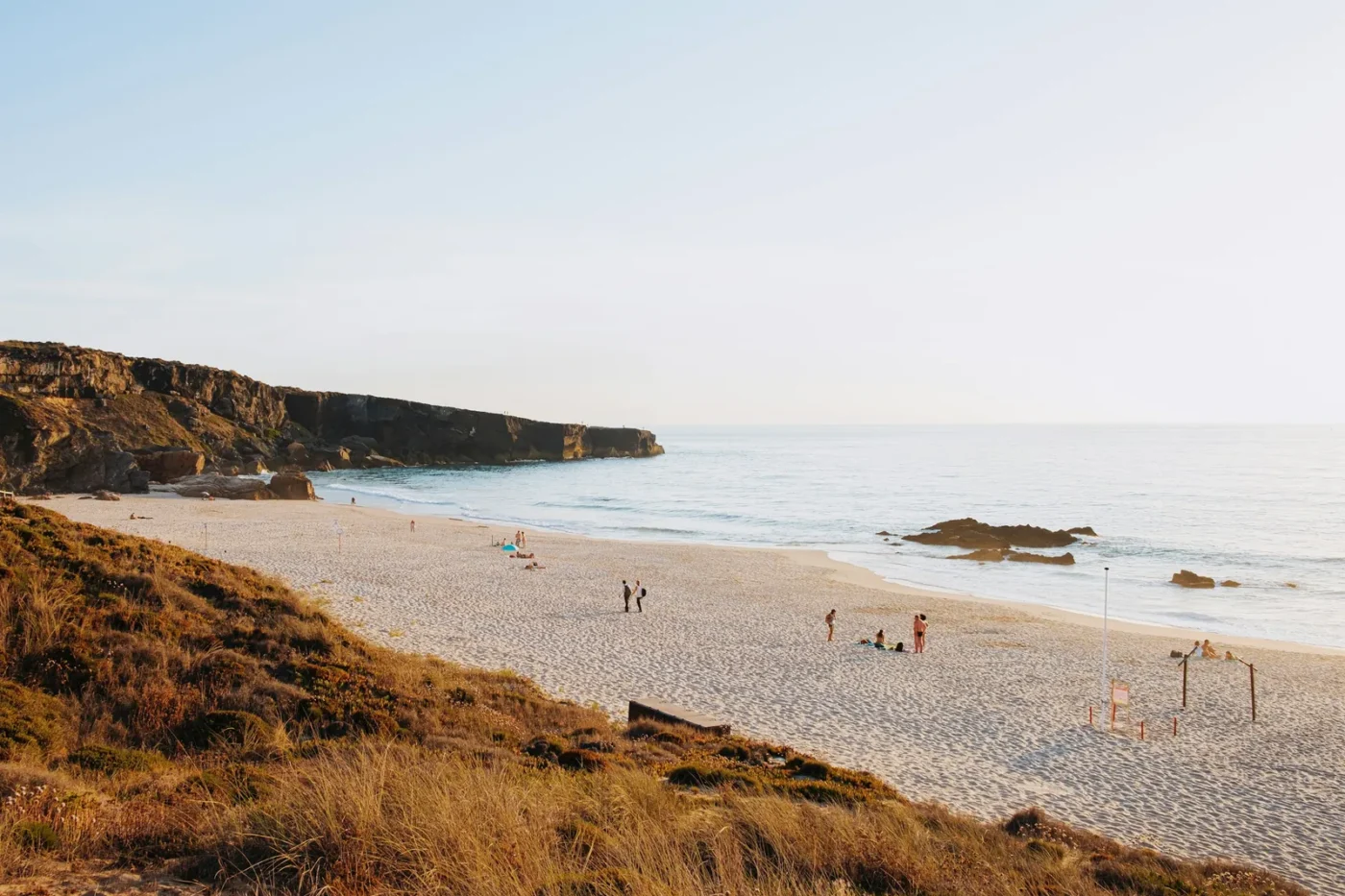 Wide sandy beach below brown cliffs on the Costa Vicentina in southwest Portugal, with dry grass on the dunes in soft light