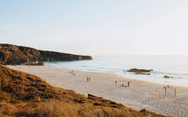 Wide sandy beach below brown cliffs on the Costa Vicentina in southwest Portugal, with dry grass on the dunes in soft light