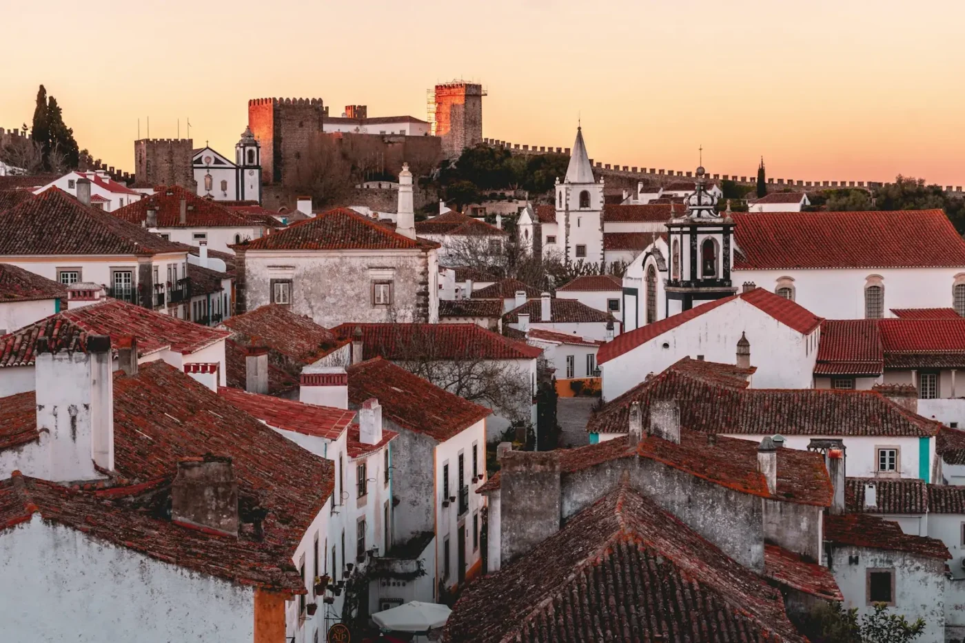 Whitewashed houses and terracotta roofs of Óbidos at sunset, with the castle and town walls rising behind them