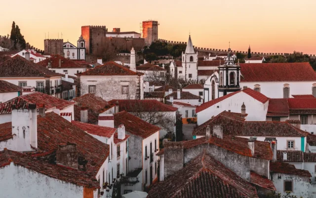 Whitewashed houses and terracotta roofs of Óbidos at sunset, with the castle and town walls rising behind them