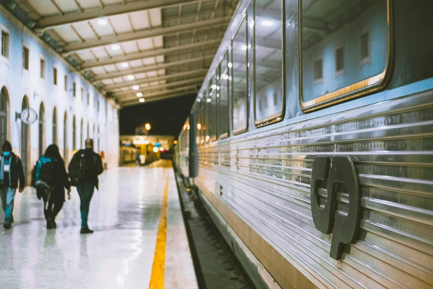 Passengers walking along a platform beside a stainless-steel CP train at Santa Apolónia station in Lisbon, Portugal