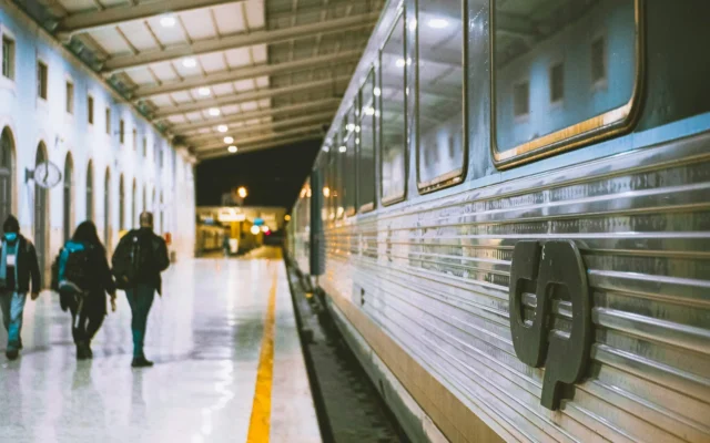 Passengers walking along a platform beside a stainless-steel CP train at Santa Apolónia station in Lisbon, Portugal