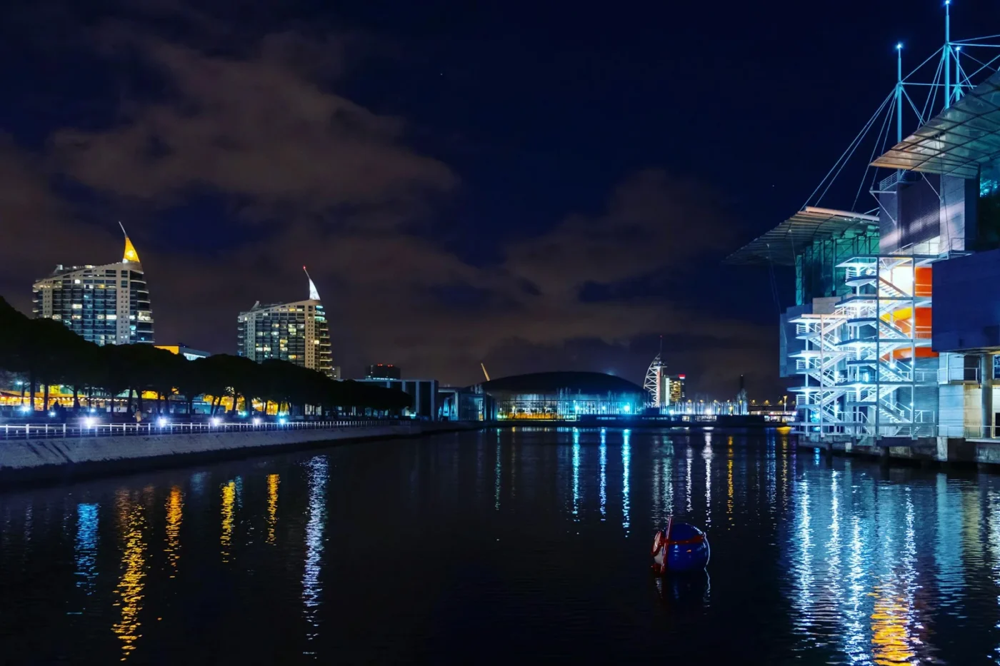 Parque das Nações waterfront in Lisbon at night, with lit towers and buildings reflected in the water near the venue